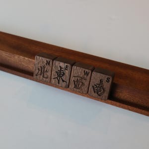 Pu&ograve; includere: Un supporto in legno marrone scuro che sostiene quattro tessere quadrate in legno. Ogni tessera presenta un carattere cinese inciso al laser che rappresenta un punto cardinale, con la corrispondente lettera inglese N, E, W o S incisa sopra.