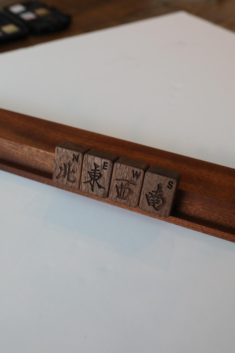 Pu&ograve; includere: Un supporto in legno marrone scuro che sostiene quattro tessere quadrate in legno. Ogni tessera presenta un carattere cinese inciso al laser che rappresenta un punto cardinale, con la corrispondente lettera inglese N, E, W o S incisa sopra.