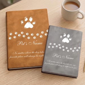 May include: Two rectangular journals, one tan and one grey, featuring white paw print graphics, the text "Pet's Name," and the quote "No matter where the day takes me, my favourite place will always be right next to you." A gold pen sits beside them.