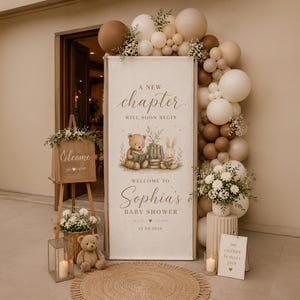 May include: A vertical banner for a baby shower featuring a teddy bear and rabbit reading books, with the text A NEW CHAPTER WILL SOON BEGIN, WELCOME TO Sophia's BABY SHOWER, and 24.08.2026. It is decorated with a balloon arch in brown and cream tones.