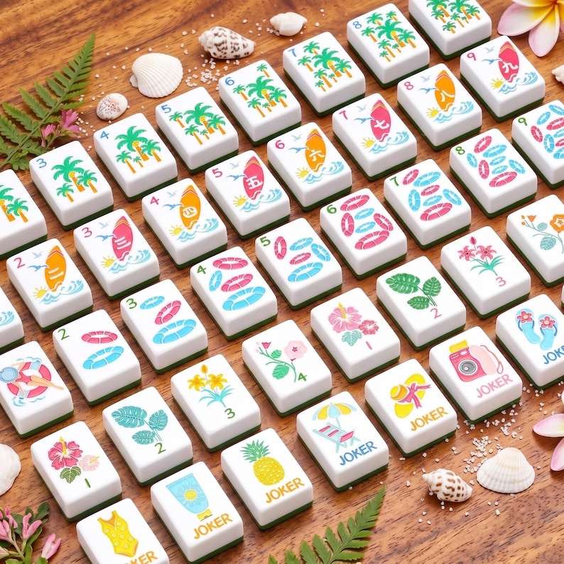 K&ouml;nnte beinhalten: Eine Sammlung wei&szlig;er Mahjong-Steine mit verschiedenen farbenfrohen Illustrationen zum Thema Sommer, darunter Surfbretter, Palmen und Blumen. Einige Steine zeigen das Wort "JOKER". Die Steine sind auf einer Holzoberfl&auml;che mit Muscheln und tropischen Blumen angeordnet.