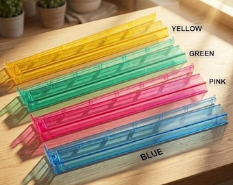 May include: Four rectangular, translucent plastic storage trays arranged in a diagonal row. The trays are colored yellow, green, pink, and blue, each labeled with its respective color name printed in black text next to it on the surface.