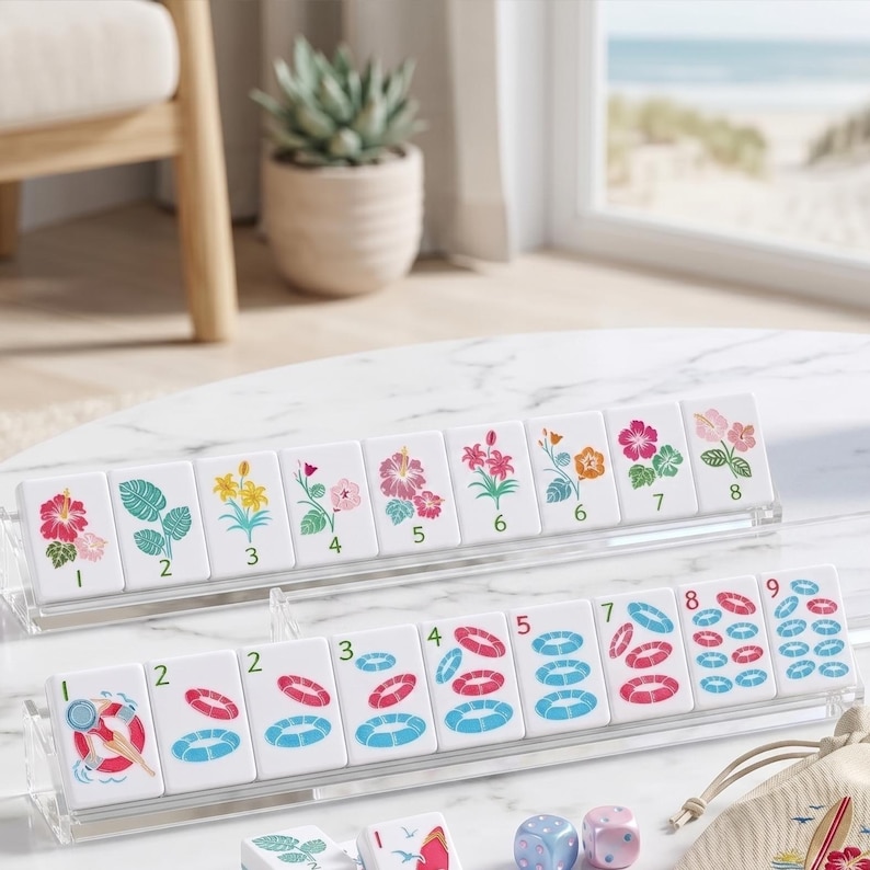 May include: A set of white Mahjong tiles with floral and water-themed illustrations, including hibiscus, leaves, and life preservers. The tiles are arranged in clear acrylic racks, with dice and a small bag visible.