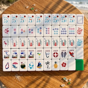Op de afbeelding: Een complete set witte Mahjong-tegels met kleurrijke illustraties. De tegels tonen diverse ontwerpen, waaronder vissen, bloemen en tropische afbeeldingen. De set bevat tegels met nummers, richtingen en Jokers, perfect voor een spelletje Mahjong.