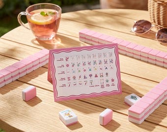 May include: A Mahjong set featuring pink and white tiles, with a pink instructional reference card displaying tile categories and symbols. The set includes rows of stacked tiles, individual tiles with colorful illustrations, and a guide card.