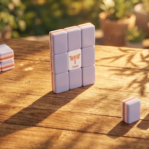 May include: A set of lavender and orange game tiles arranged on a wooden surface. The tiles are rectangular with a dragonfly graphic and the word "CRAK" on one tile. Additional tiles are stacked and scattered nearby.