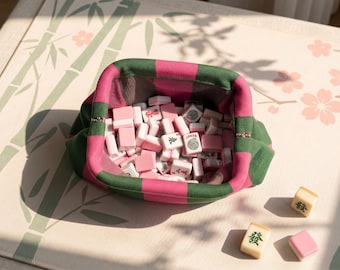 May include: A fabric pouch with a pink and dark green checkered pattern containing a collection of small, rectangular mahjong tiles. The tiles are primarily pink and white, with some featuring green symbols and the word Joker printed on them.