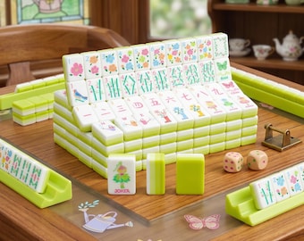 May include: A complete Mahjong set with white tiles featuring green edges and colorful floral and character designs. The set includes dice, tile racks, and a wooden game table. The tiles are stacked in a display.