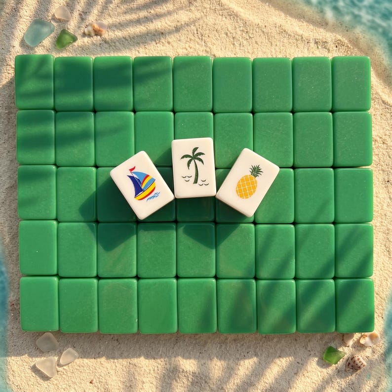 Op de afbeelding: Groene rechthoekige tegels gerangschikt in een raster met drie witte tegels met een zeilboot, palmboom en ananas. De tegels liggen op zand, met de zee op de achtergrond.