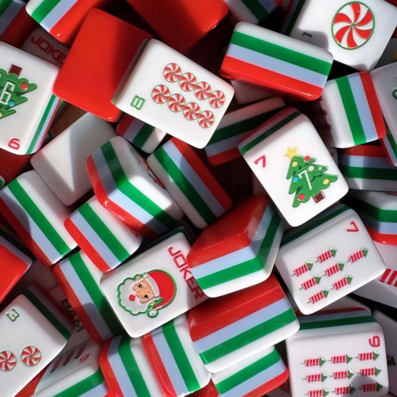 May include: A collection of Christmas-themed Mahjong tiles. The tiles feature red, white, and green colors, with images of candy canes, Christmas trees, and Santa Claus. Some tiles have numbers and the word "Joker".