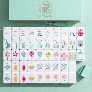 May include: A mint green box set of Mahjong tiles. The tiles are white with colorful illustrations and Chinese characters. The box has the text "MINT DRAGON" and a gold dragon emblem.