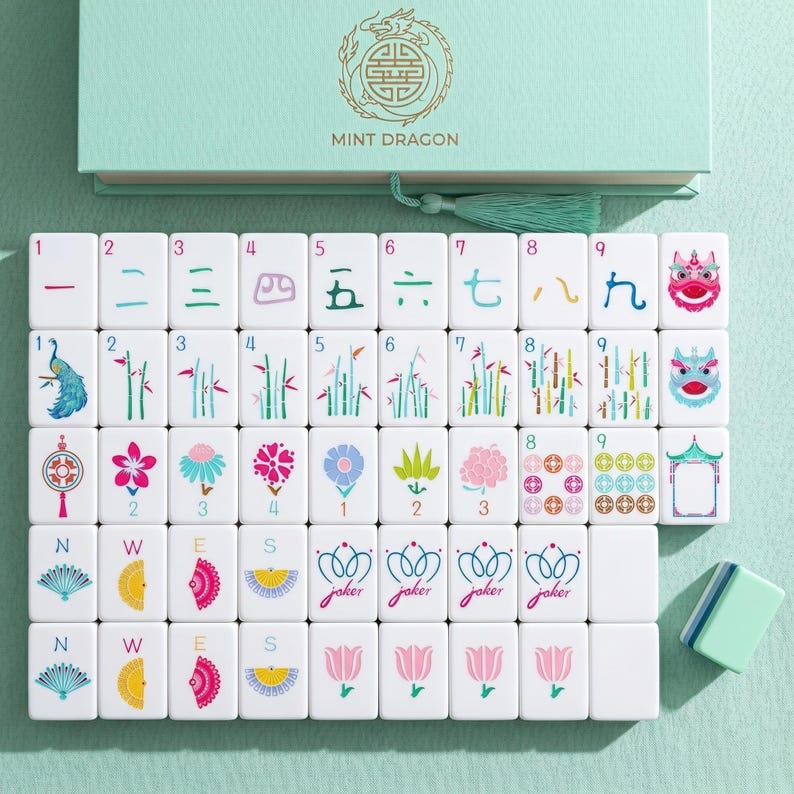 May include: A mint green box set of Mahjong tiles. The tiles are white with colorful illustrations and Chinese characters. The box has the text "MINT DRAGON" and a gold dragon emblem.