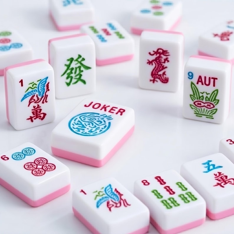 May include: A collection of white Mahjong tiles with pink bases, featuring various colorful engraved symbols, Chinese characters, and the word JOKER in red text. The tiles display numbers, dragon motifs, and floral patterns in blue, green, and red ink.