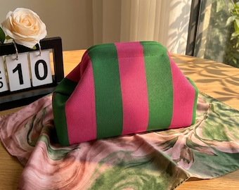 May include: A structured pouch featuring a bold vertical striped pattern in vibrant hot pink and forest green. The bag has a curved top opening and a textured, woven fabric construction, presenting a clean, geometric shape with a distinct color contrast.