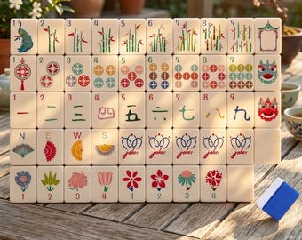 May include: A set of off-white mahjong tiles arranged in a grid, featuring colorful illustrations of bamboo, circles, Chinese characters, wind directions, flowers, and joker symbols. A single blue and white tile sits separately on the wooden surface.