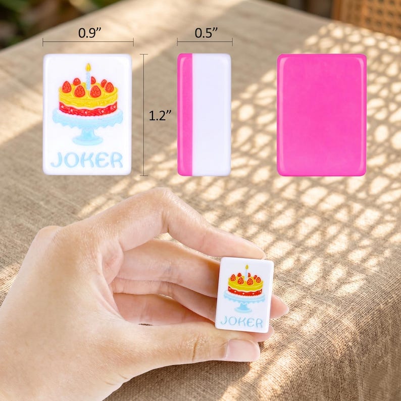 May include: A set of rectangular game pieces. One piece features a cake design with a candle and the word "JOKER". The dimensions are 0.9" x 1.2" x 0.5". The other pieces are solid pink and white. One piece is held in a hand.