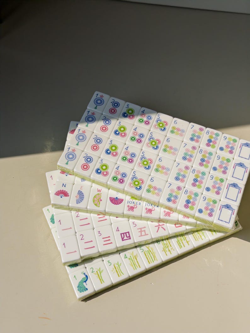May include: A set of white rectangular Mahjong tiles arranged in three overlapping rows. The tiles feature colorful printed designs including numbers 1 through 9, directional symbols, bamboo stalks, peacock illustrations, and the text JOKER.