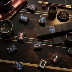 May include: A set of black mahjong tiles with neon-colored engravings, including a tile labeled JOKER, scattered on a dark wood surface with gold inlay. The set includes small ceramic cups, a burning incense coil, and a pair of wooden chopsticks.