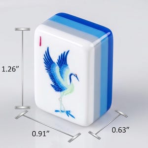 Puede incluir: Una ficha de Mahjong blanca y azul con una ilustraci&oacute;n de una grulla azul. La ficha mide 3,2 cm de alto, 2,3 cm de ancho y 1,6 cm de grosor. El borde superior tiene rayas azules y grises.