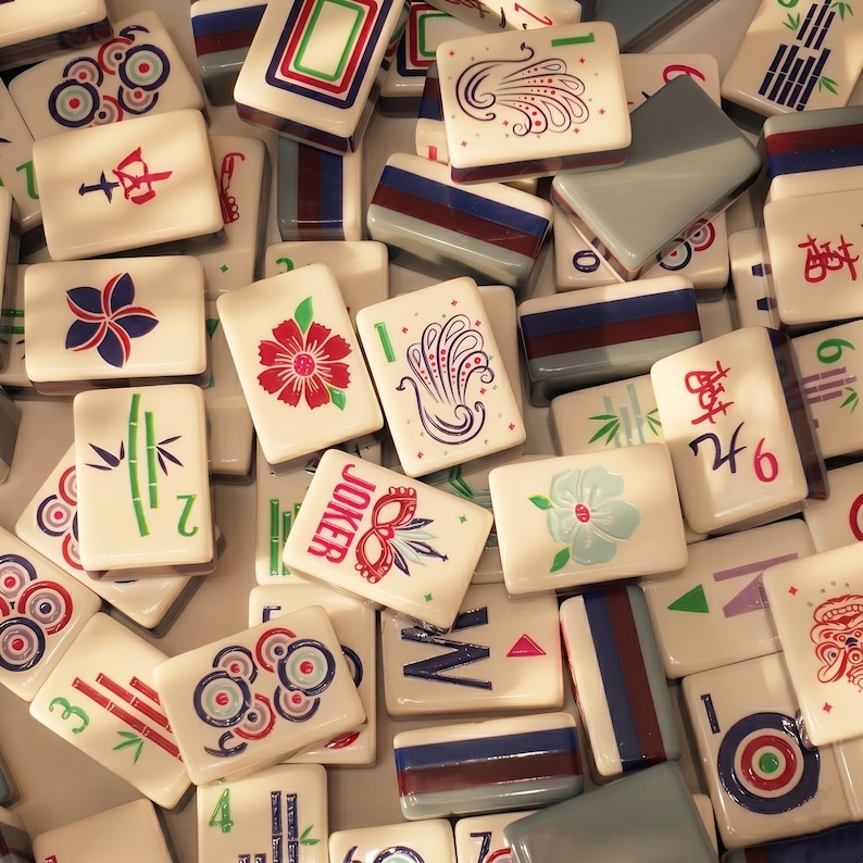 May include: A collection of ivory-colored Mahjong tiles with various colorful designs and symbols. The tiles feature illustrations of flowers, bamboo, and geometric patterns, along with Chinese characters and the word "JOKER". The tiles are arranged in a close-up, overhead shot.