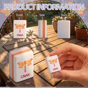May include: White and orange tile with a dragonfly design and the word "CRAK". The tile is rectangular, measuring approximately 1.26 inches tall, 0.94 inches wide, and 0.6 inches thick. The dragonfly is yellow and red.