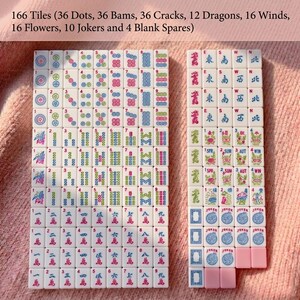 May include: A complete Mahjong tile set with 166 tiles, including dots, bams, cracks, dragons, winds, flowers, jokers, and blank spares. The tiles are white with colorful symbols and characters. The set is displayed on a pink surface.