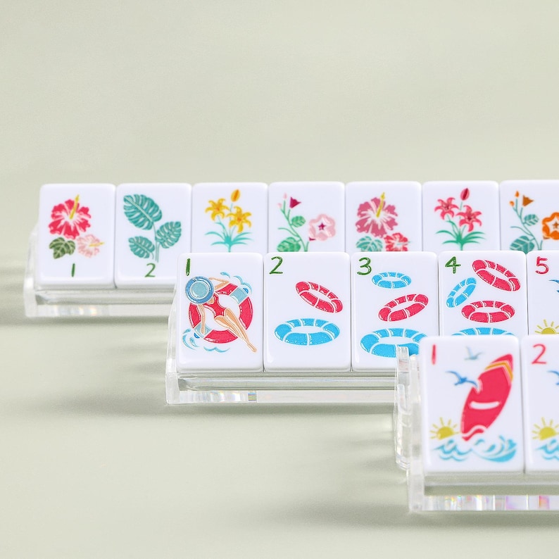 K&ouml;nnte beinhalten: Eine Reihe wei&szlig;er Spielsteine mit farbenfrohen Illustrationen, darunter Blumen, eine Person in einer Schwimmboje und ein Surfbrett. Die Spielsteine sind auf transparenten Acrylst&auml;ndern angeordnet.