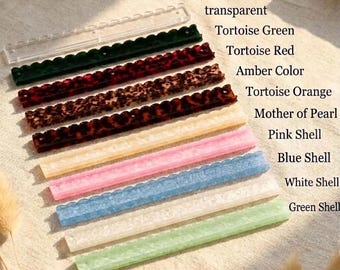 May include: A collection of ten long, thin, rectangular strips with scalloped edges, labeled as transparent, Tortoise Green, Tortoise Red, Amber Color, Tortoise Orange, Mother of Pearl, Pink Shell, Blue Shell, White Shell, and Green Shell.