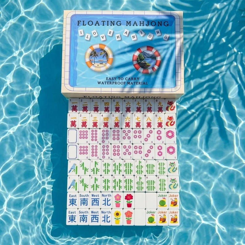 May include: A Floating Mahjong game set featuring a rectangular box with the text "FLOATING MAHJONG" and "I LOVE MAHJONG" above two life preserver graphics. Below the box, a grid of white Mahjong tiles displays various characters, symbols, and colors.