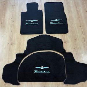 Puede incluir: Un juego de tres alfombrillas negras para coche con el logotipo y el texto Thunderbird bordados en azul claro. El juego incluye dos alfombrillas delanteras rectangulares y una alfombrilla trasera grande de forma única con bordes.