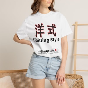 Könnte beinhalten: Ein weißes kurzärmeliges T-Shirt mit großen schwarzen japanischen Kanji-Zeichen mit roter Umrandung, dem Text "Shitting Style" in Schwarz und dem Schriftzug "JAPANGLISH FUNNY TRANSLATIONS. SERIOUSLY." mit einem kleinen japanischen Flaggensymbol.