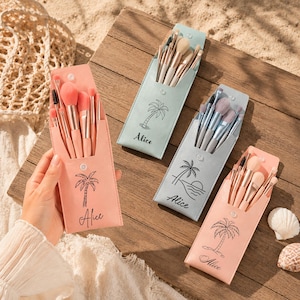 Op de afbeelding: Vier sets make-up kwasten in pastelkleurige kunstlederen etuis, elk voorzien van een palmboomafbeelding en de naam Alice. De etuis in lichtroze, mintgroen en lichtblauw bevatten diverse kwasten met metalen handvatten.