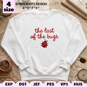 May include: A white crewneck sweatshirt featuring red embroidered text that reads the last of the bugs, positioned above a small red and black ladybug embroidery. The design is available in 4, 5, 7, and 9 inch sizes for digital embroidery.
