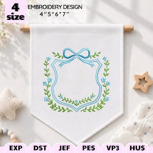 May include: A white fabric banner featuring an embroidered light blue shield-shaped frame topped with a bow, surrounded by green vines and small blue flowers. The text reads 4 size EMBROIDERY DESIGN 4" 5" 6" 7". File formats include EXP, DST, JEF, PES, VP3, and HUS.