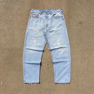 Könnte beinhalten: Hellblaue Jeans aus Denim im klassischen Fünf-Taschen-Design mit Knopf- und Reißverschluss sowie einem Used-Look mit ausgefransten Kanten an Bund, Taschen und Säumen sowie mehreren horizontalen Rissen auf den Vorderseiten der Hosenbeine.