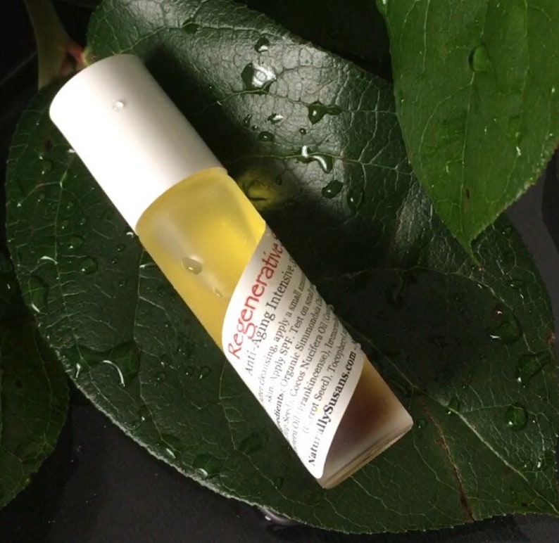 May include: A white and brown glass roll-on bottle with a label that reads "Regenerative Anti-Aging Intensive". The bottle is on a green leaf with water droplets.