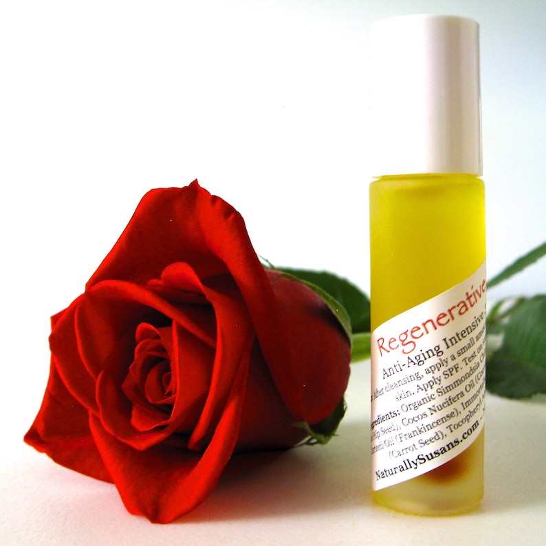 May include: A clear glass bottle with a white cap and a yellow liquid inside. The bottle has a label that reads "Regenerative Anti-Aging Intensive". The bottle is next to a red rose.