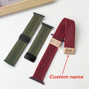 Puede incluir: Dos correas de reloj tejidas con un patrón de diamantes texturizado. Una correa es de color verde oliva con herrajes negros y la otra es de color rojo oscuro con herrajes en oro rosa. La correa roja tiene una placa grabada con "lisa".