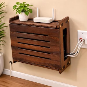 Può includere: Una scatola portaoggetti da parete in legno marrone scuro con doghe orizzontali sul pannello frontale. La superficie superiore ospita una piccola pianta in vaso bianca e un router wireless bianco. I cavi escono dal lato verso una presa.