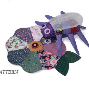 Peut inclure: Une fleur en patchwork violet et blanc avec un insecte violet et blanc sur le dessus. L'insecte a une aile blanche transparente et un œil bouton. La fleur a un bouton brun au centre.