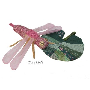 Peut inclure: Une libellule en tissu rose et vert avec une feuille en patchwork. La libellule a un motif paisley et un grand œil. La feuille est faite de différents tissus verts et roses.