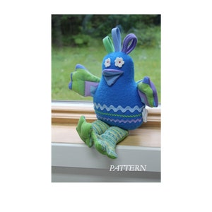 May include: A blue and green plush toy bird with white eyes and a purple crest. The bird is sitting on a windowsill with its legs crossed.