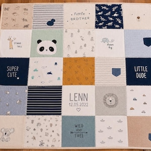 Könnte beinhalten: Eine quadratische Patchwork-Decke bestehend aus fünfundzwanzig Stoffquadraten mit verschiedenen Mustern und Illustrationen, darunter ein Panda, ein Löwe, ein Koala und eine Giraffe. Der Text umfasst "little BROTHER", "SUPER CUTE", "LITTLE DUDE", "LENN 12.05.2022" und "WILD AND FREE".