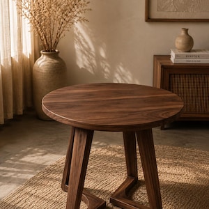 May include: A round, dark brown wooden side table with a smooth surface. The table has three angled legs, creating a sturdy base. The table is approximately 20 inches in diameter and 18 inches tall, perfect for a living room or bedroom.