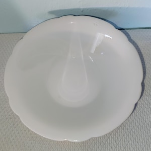 Puede incluir: Un tazón de cerámica blanco con un borde festoneado. El tazón tiene una pequeña hendidura en el centro.