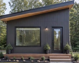 May include: A small, modern cabin with dark vertical siding and a single-slope roof. The exterior features a large rectangular window, a glass-paneled door, and a wooden deck with steps. Three potted evergreen shrubs sit along the front porch.