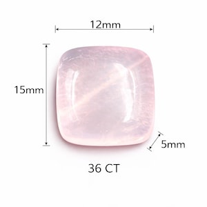 May include: A pale pink, square-shaped gemstone with rounded corners. The stone is labelled with dimensions of 12mm by 15mm by 5mm and a weight of 36 CT. The surface of the stone is smooth and translucent, showing internal crystalline textures.