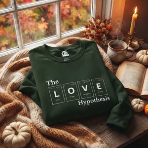 Puede incluir: Una sudadera de manga larga de color verde oscuro con un estampado gráfico blanco de elementos de la tabla periódica que deletrean The LOVE Hypothesis. El diseño incluye símbolos químicos, cuello redondo y puños acanalados.