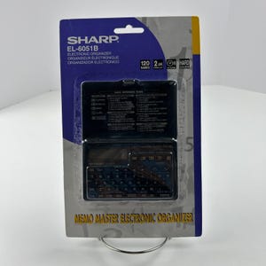 Puede incluir: Un nuevo organizador electrónico Sharp EL-6051B en su embalaje original. El embalaje es azul y amarillo, con el nombre del producto y sus características impresas en la parte delantera. El organizador tiene un teclado pequeño y una pantalla de dos líneas.