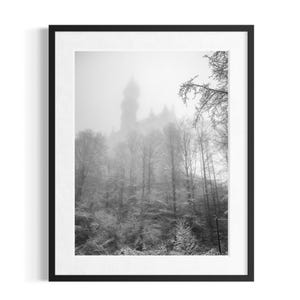 Può includere: Una stampa artistica da parete incorniciata in bianco e nero che raffigura un'alta torre di un castello parzialmente oscurata da una fitta nebbia. In primo piano si vede un fitto bosco di alberi spogli coperti da un leggero strato di neve.